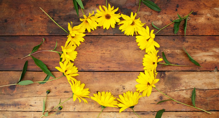 A Circle of yellow daisies on a wooden table with a mug of tea in the middle