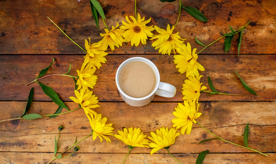 a Circle of yellow daisies on a wooden top with a mug of tea in the middle