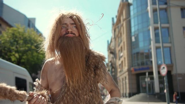 Ancient discoverer wildman in animal fur exploring future city architecture modern civilization with great surprise. Timetraveling.