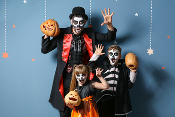Father with children in Halloween costumes and with pumpkins on color background