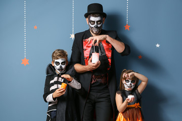 Father with children in Halloween costumes and with candles on color background