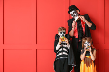 Father with children in Halloween costumes eating cookies on color background