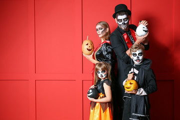 Family in Halloween costumes and with pumpkins on color background