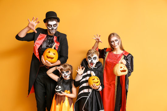 Family in Halloween costumes and with pumpkins on color background