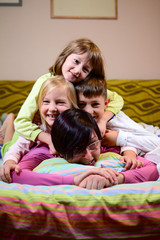 A mother of three plays with her children in the morning after bedtime. children love playing in the morning with their mother until they are up. The concept of a healthy sleepy family. Vertical.
