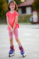 Little girl riding on roller skates outdoor. Happy young girl learning to rollerblade. Kid wearing...