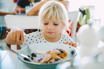 Little blonde girl eating pancakes in a cafe