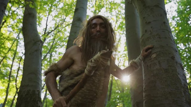 Caveman of neanderthals homo sapiens with survival spear exploring virgin forest nature discovering camera on ground. Curious portrait.