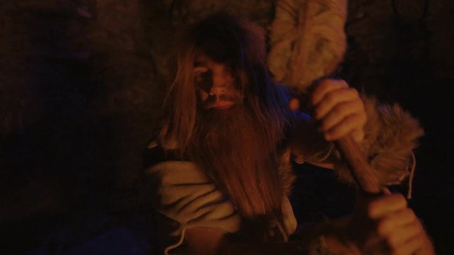 Neanderthal of stone-age period covered in hair holding survival spear telling scary story in cavern at bonfire. Mysterious life of cave dweller. Homo sapiens.