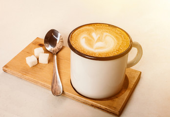 Cup of latte coffee with foam from above, spoon and sugar on white background.
