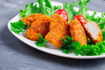 A part of a white plate with delicious fresh fried golden chicken nuggets with crisp, three cherry tomatoes, lettuce and parsley.