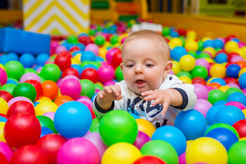 Playground with ball pit indoor. Joyful small kid having fun at indoor play center. Child is playing with colorful balls in playground ball pool. Holiday or birthday