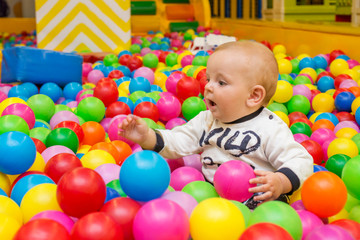 Playground with ball pit indoor. Joyful small kid having fun at indoor play center. Child is playing with colorful balls in playground ball pool. Holiday or birthday