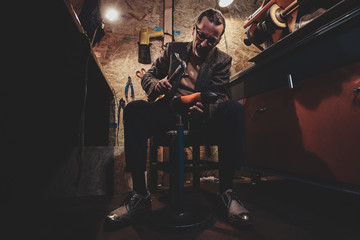 Focused mature cobbler is fixing sole for boots using hammer.