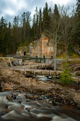 Fototapeta na wymiar Sandstone rock with caves and an old Floodgate Dam , Ligatne, Latvia.