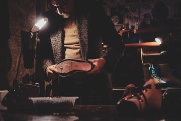 Elderly boots maker is working on his new shoe collection at workshop.