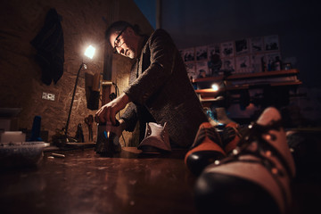 Elderly person is serving boot service at his own personal workshop.