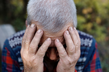 Depressed old man hiding his face behind hands. Adult man has a headache.