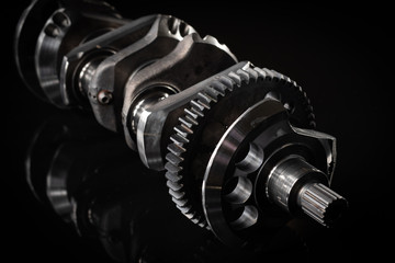 high performance factory racing crankshaft. set on a black reflective background with different lighting.