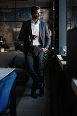 Young handsome businessman stand and hold glass of whiskey in his own office.