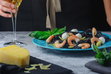 Black spaghetti with cuttlefish ink. Shrimp pasta with mozzarella and basil. Cropped photo of a girl with a glass of wine.