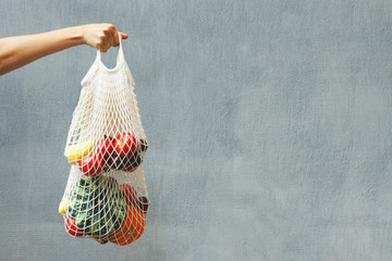 Hand with an eco bag on a gray background. Place for text. Zero waste concept, plastic-free,...