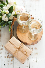 Glasses with wine on a white rustic wooden background with a bouquet of flowers and craft gift. Wedding table greeting card. Wedding invitation light background.