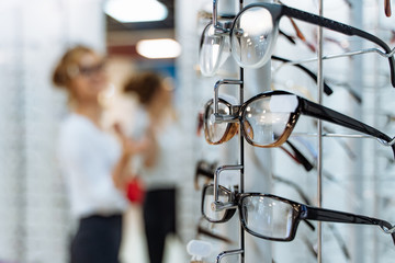 Eyeglasses shop. Stand with glasses in the store of optics. Woman chooses glasses.