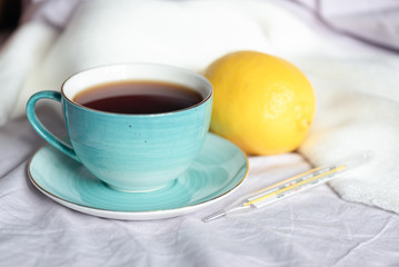 Cup of tea with fresh lemon and a thermometer with high body temperature.
