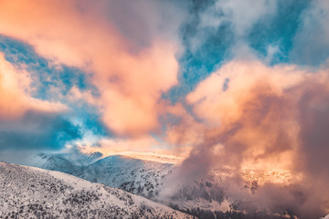 Mountains covered with snow. Beautiful winter landscape during sunset. Blue sky and golden rays of the sun through the clouds