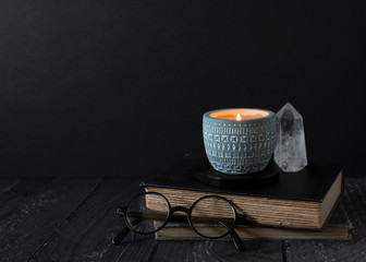 candle burning on stacked books, reading glasses, crystal, antique books, burning scented candle in pretty blue ceramic holder, copyspace, dark background with copy space, autumn mood