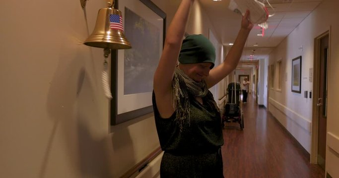 Young woman ringing a bell for finishing her last chemotherapy treatment