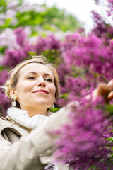 Fototapeta premium Beautiful blond woman posing outdoors at the blur spring park of violet and white lilac background