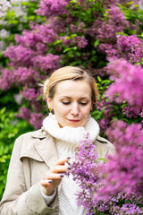 Beautiful blond woman posing outdoors at the blur spring park of violet and white lilac background