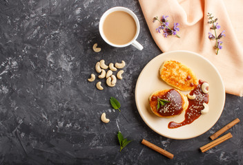 Cheese pancakes with caramel sauce on a beige ceramic plate and a cup of coffee on a black concrete...