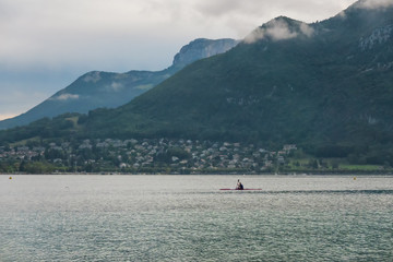 Fototapeta premium Morning landscape on Lake Annecy, France. In the background are the mountains of the Alps. On the lake in the distance you can see the silhouette of a man kayaking.