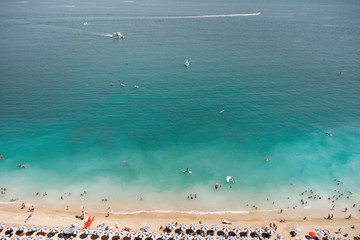 Aerial view of sandy beach with tourists swimming in beautiful clear sea water and yacht from top view.