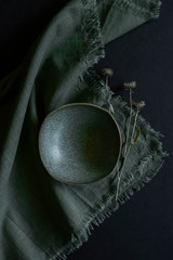 green handmade bowl with green cloth napkin and dried thistle flowers on black table, pottery workshop, hand crafted dish with dried flower on dark background, empty green bowl