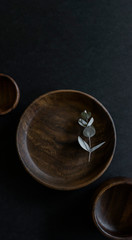 wooden dishes with green cloth napkin and eucalyptus leaves on dark counter, collection of teak dishes at craft fair, beautiful wood bowls and plate on black background, copyspace, copy space