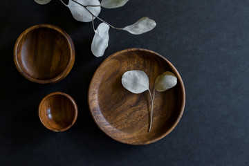 wooden dishes with green cloth napkin and eucalyptus leaves on dark counter, collection of teak...