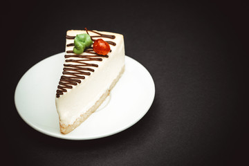 a piece of cheesecake decorated with a cherry on a ceramic white plate top view on a dark background selective focus