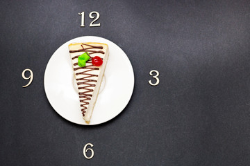 slice of cheesecake and time alphabet letters clock 3 6 9 12 break ceramic white plate top view height plan on dark background