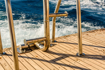 Metal staircase for descent into the water and wave trace with white foam on a water surface behind...