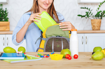 Closeup of mother packing lunch box into a kids backpack