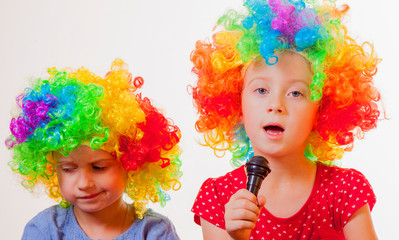 Portrait of little cute caucasian child girls superstars singing with the microphone. Funny facial expression.
