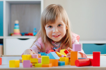 Smiling little girl playing with color wooden blocks