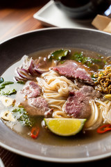 Close up of raw beef tenderloin soup with rice noodles, onion, garlic, chilli pepper, seedlings and mint in daylight