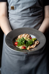 Waiter is holding classic caesar salad with grilled chicken fillet, greens and cherry tomatoes in daylight