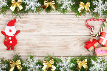 Christmas frame made of fir branches decorated with snowflakes and bows on a light wooden background