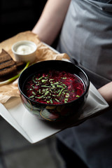 Waiter is holding a tray with ukrainian borscht served with lard slices, rye toasts, green onion...